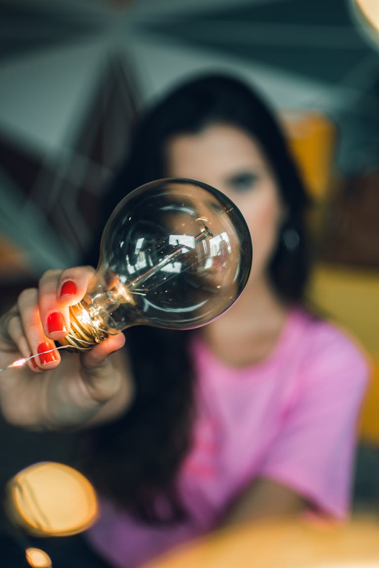 Woman showcasing a clear lightbulb indoors, emphasizing creativity and focus.